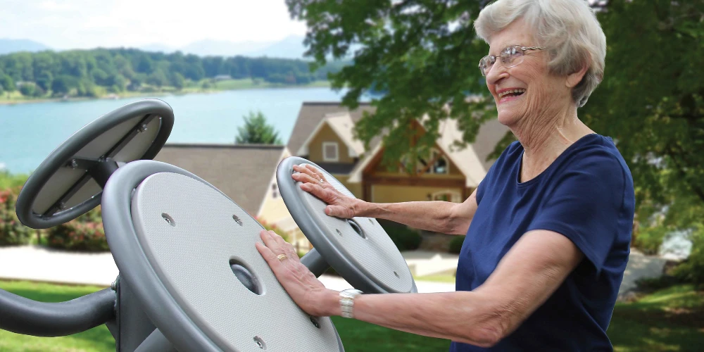 Senior woman using accessible outdoor fitness station for low-impact exercise in a park setting